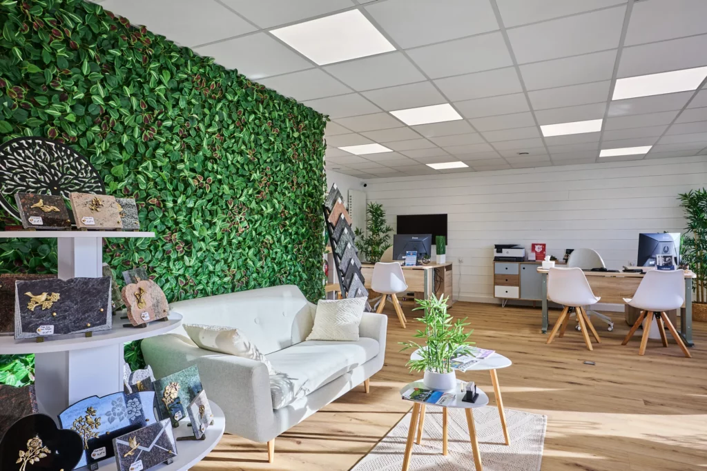 Espace d'accueil lumineux de l'agence de pompes funèbres avec mur végétal et plaques funéraires.