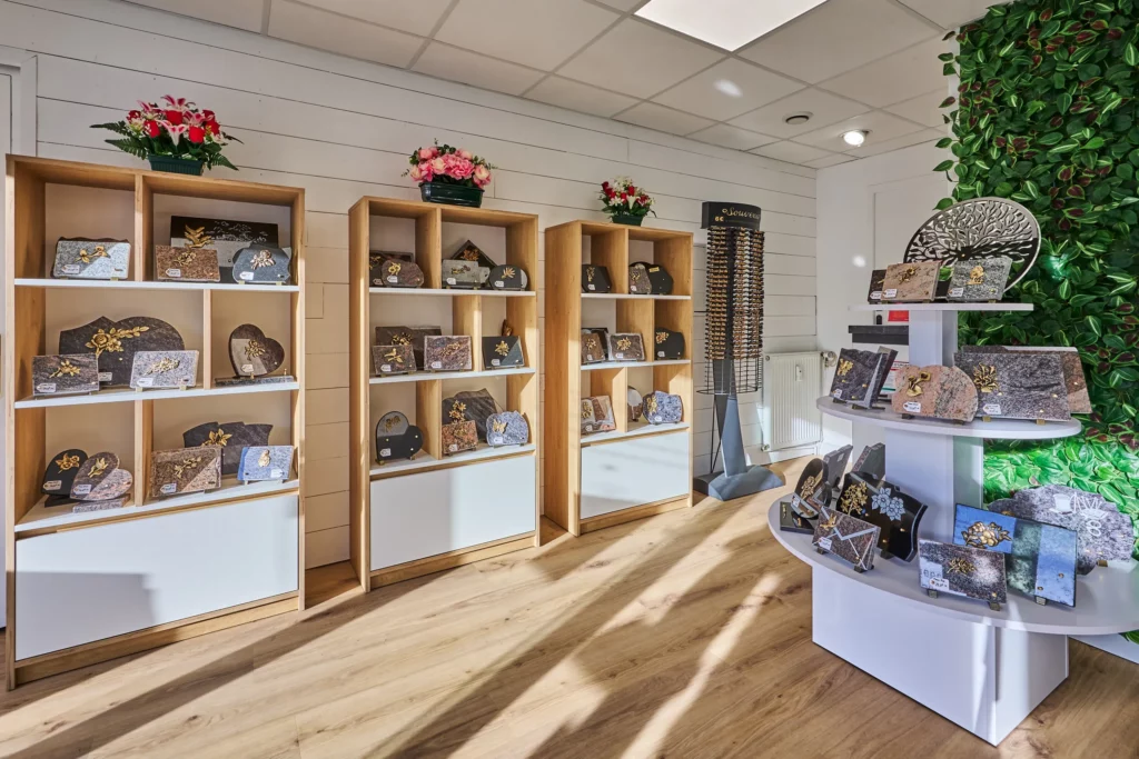 Exposition de plaques funéraires en granite et articles du souvenir sur des étagères en bois.