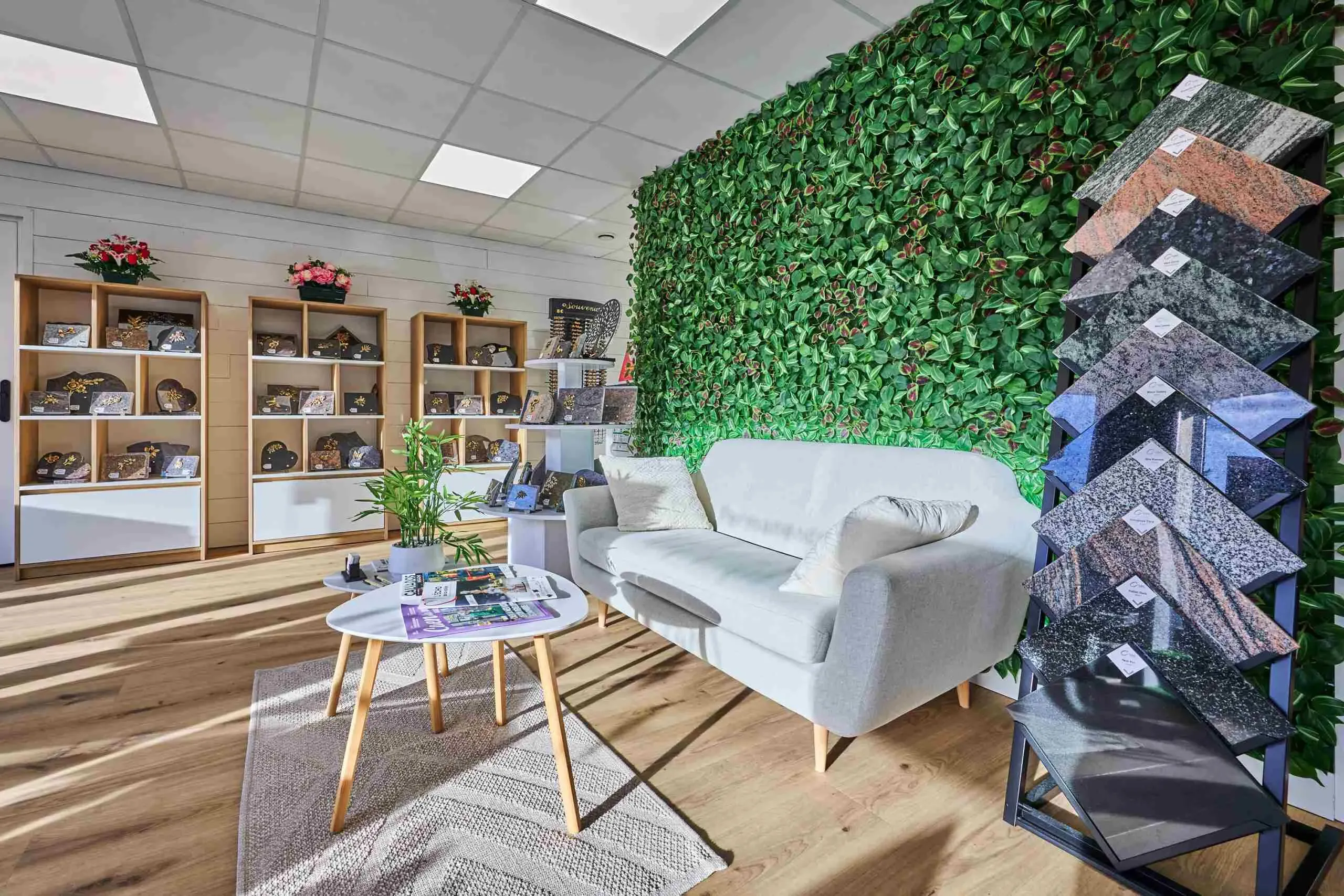 Salon d'accueil moderne avec canapé, mur végétal et présentoir d'échantillons de granite.