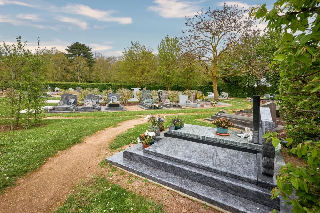 Monuments funéraires en granite installés dans un cimetière paysager bordé d'arbres.